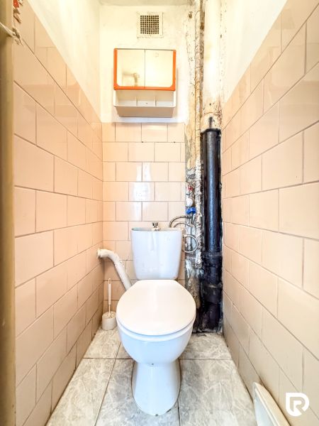 WC with beige tiles in a 3-room apartment, simple design, white toilet.