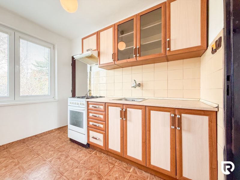 A kitchen with wooden cabinets, a wooden-patterned floor, and a stove in a 3-room apartment.