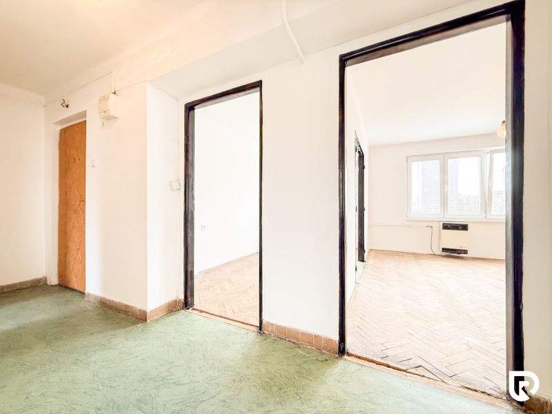 A hallway with a wooden decor floor and a view of a room in a 3-bedroom apartment.