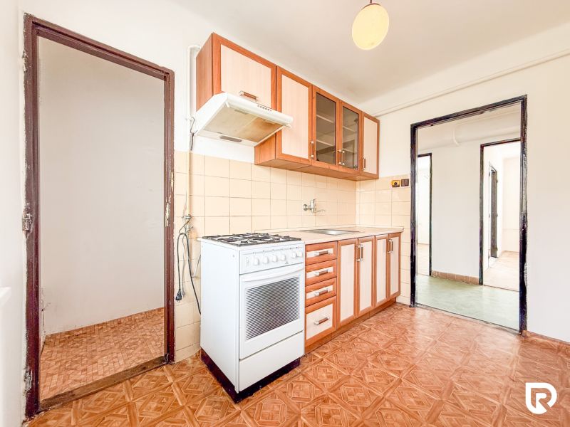 A kitchen in a 3-room apartment with a wood-patterned floor and light-colored furniture.
