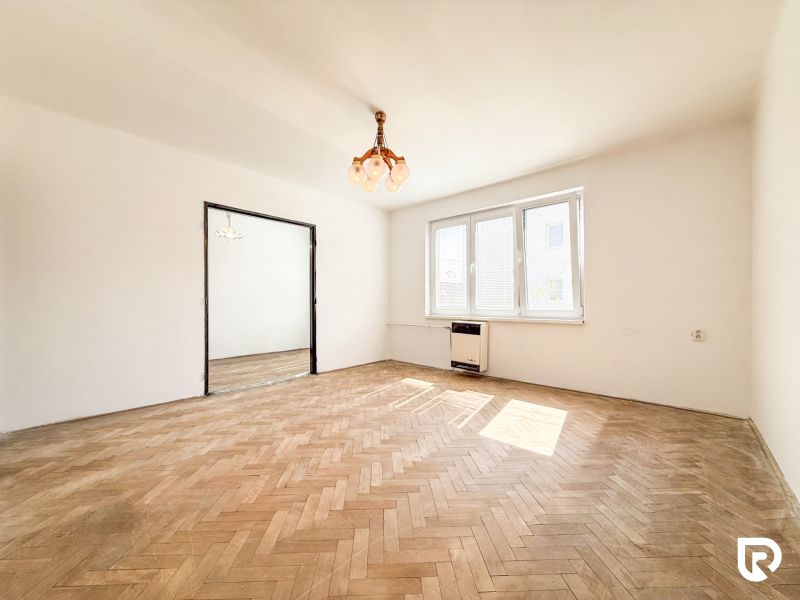 A bright room with wood-patterned flooring in a three-room apartment, large windows.