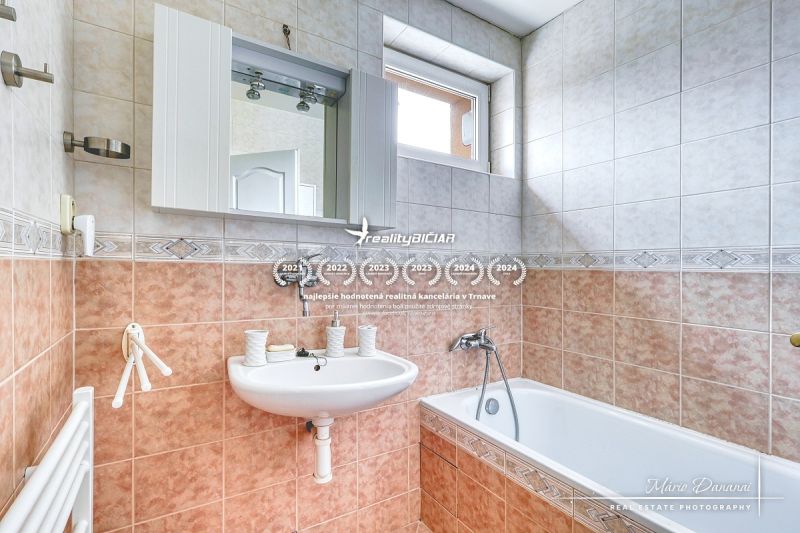 A bathroom in a family house with a sink, mirror, bathtub, and a window above the door.