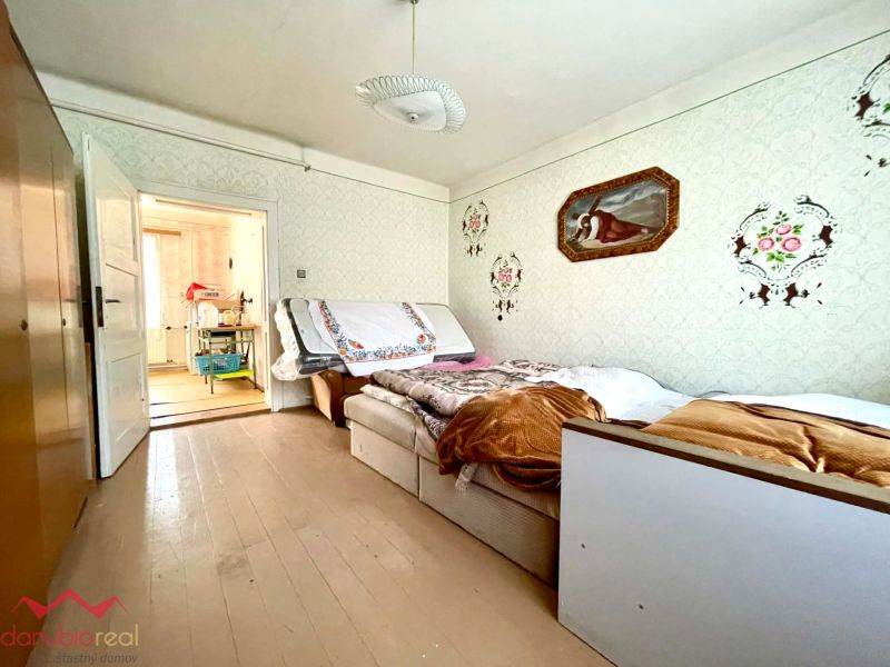 A room in a family house with a wooden decor floor, a bed, and paintings on the wall.