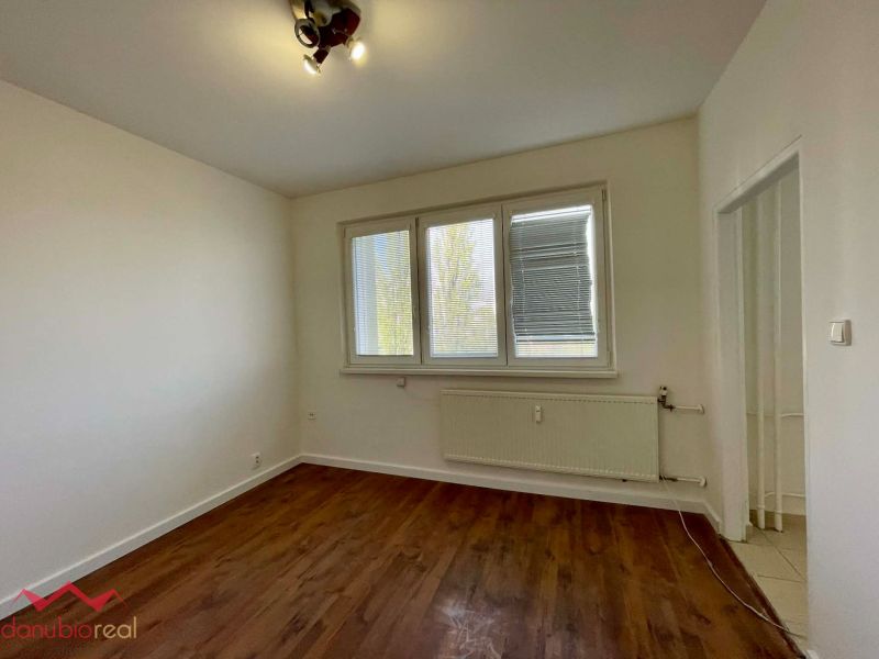A room with a wooden decor floor in a one-room apartment, light walls, and a radiator.