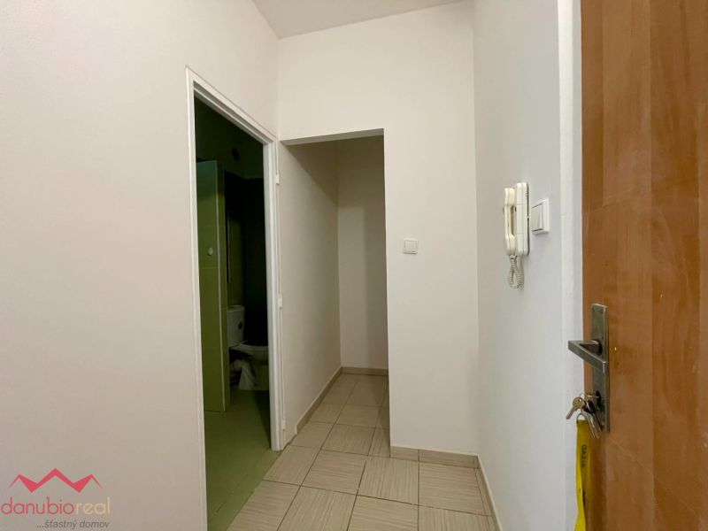 Entrance hallway with tiles, white walls, and an intercom in a studio apartment.