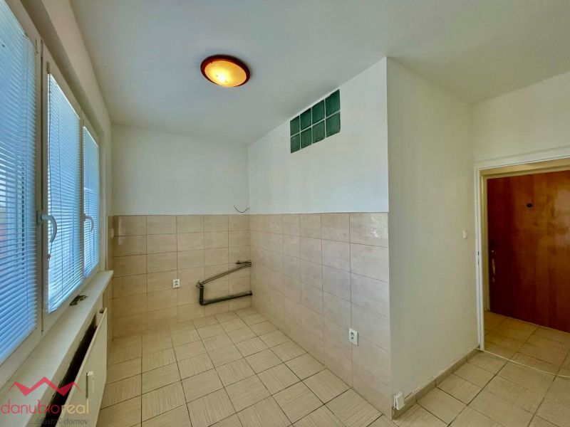 An empty kitchen area with light tiles in a studio apartment.
