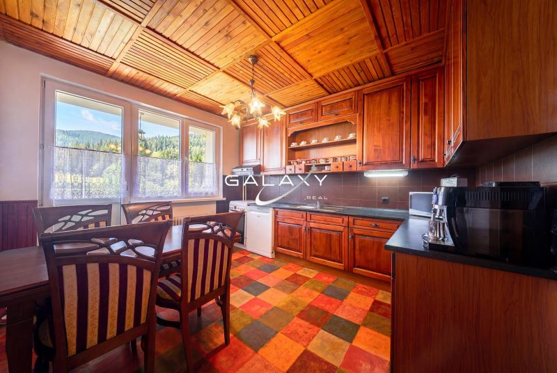 A kitchen in a family house with wooden cabinets, a colorful floor, and a view of the forest.