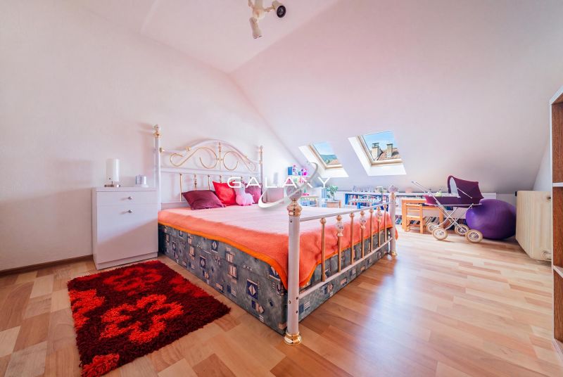 Attic room with a bed and skylights, in a family house, with a floor featuring a wooden decor.