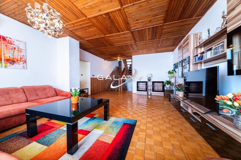 Living room of a family house with a sofa, wood-patterned flooring, and a wooden ceiling.