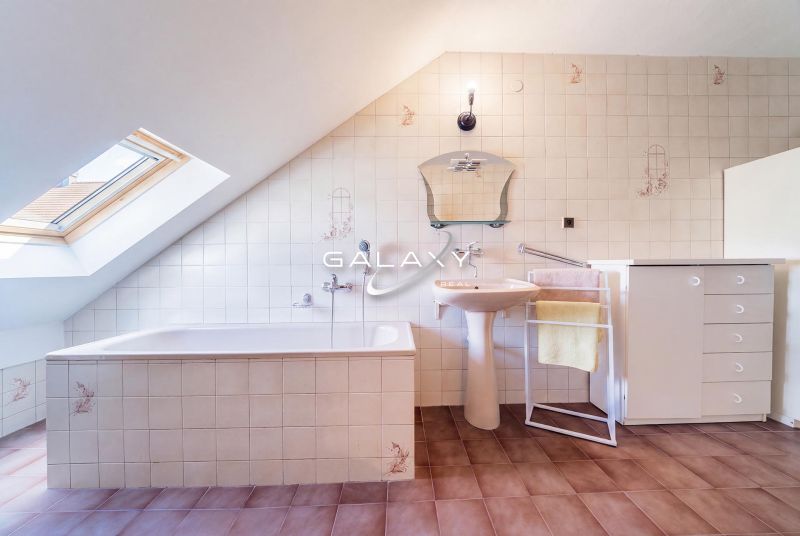An attic bathroom in a family house with a bathtub, a sink, and a skylight.
