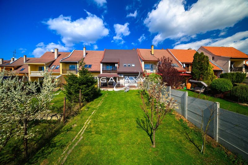 A family house in Rimavská Sobota with a garden, lawn, and flowers, blue sky.