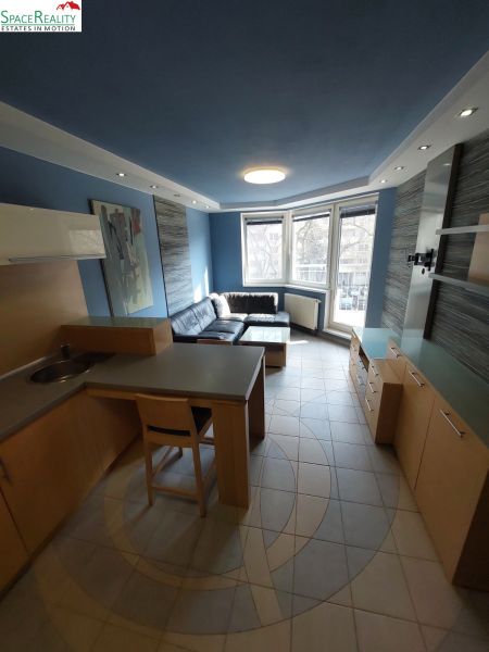 A living room with blue walls, a kitchenette, and a corner sofa in a 2-room apartment.