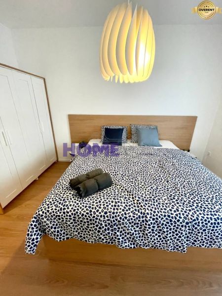 Bedroom in a 3-room apartment with a wood-patterned floor, patterned bed linen, and a modern light fixture.