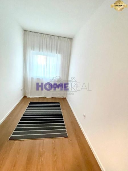 A narrow room with a wooden decor floor and a striped carpet in a 3-room apartment.