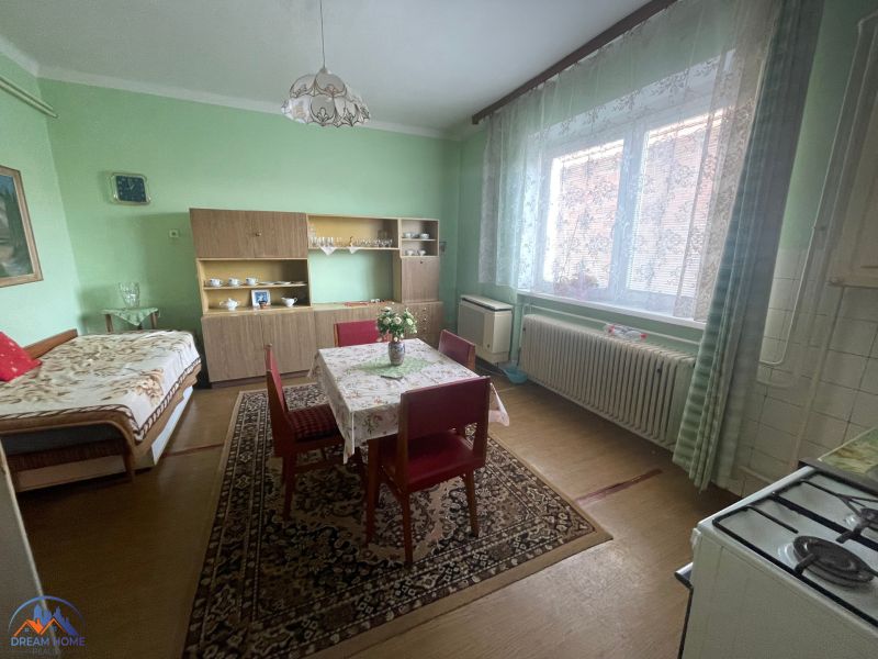 Green wall with furniture, dining table, bed in a family house with wood-patterned flooring.