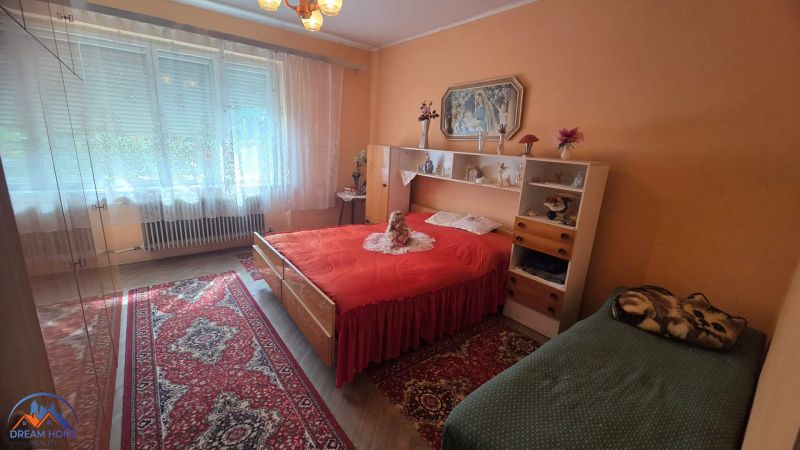 A bedroom in a family house with an oriental rug and a bed with a red blanket.