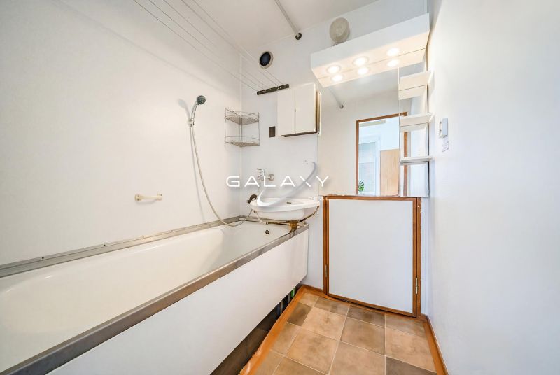 Bathroom with a bathtub and shower in a 2-room apartment, floor with wooden decor.