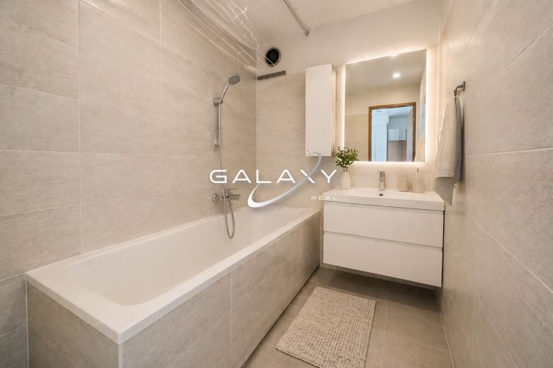 Bathroom in a 2-room apartment with a bathtub, sink, and light tiles.