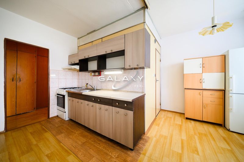 A kitchen in a 2-room apartment with a wood-patterned floor and a simple kitchen unit.