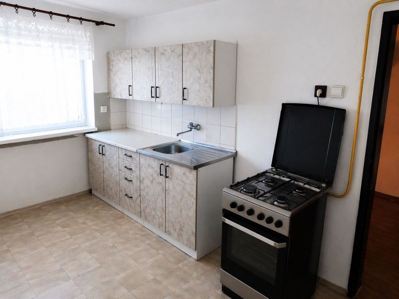 Kitchen in a 3-room apartment with a gas stove and curtains, floor with wood decor.