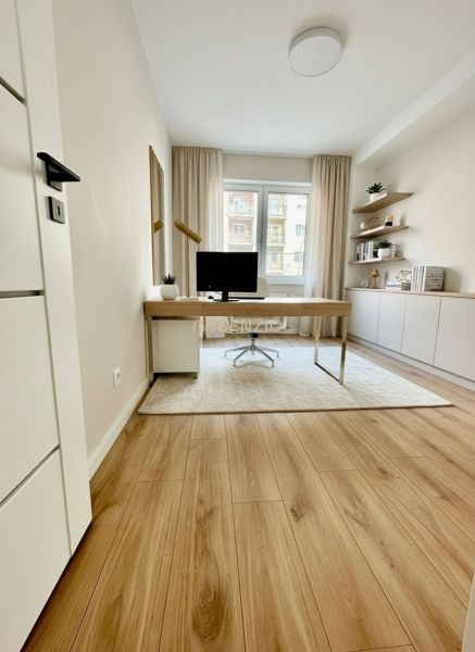 A bright study in a 4-room apartment with a wooden decor floor and a desk.