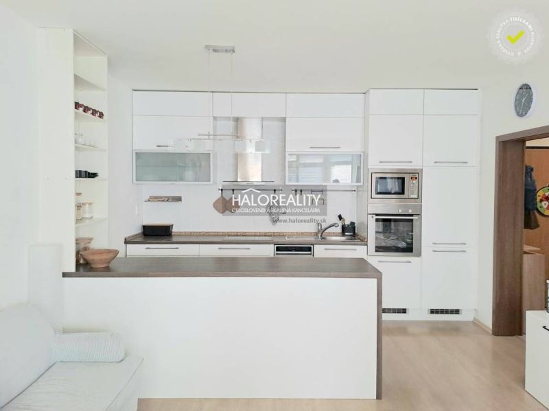 A kitchen with white cabinets and built-in appliances in a 2-room apartment, with a wood-patterned floor.