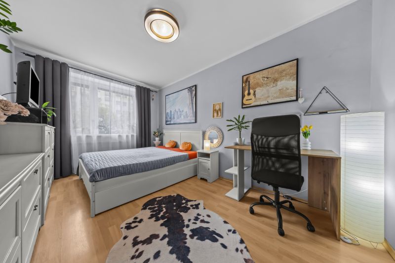 Bedroom in a three-room apartment with a wood-patterned floor, a desk, and a decorative rug.
