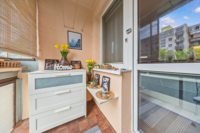 A balcony in a 3-room apartment with a chest of drawers, decorations, and a view of the apartment building.