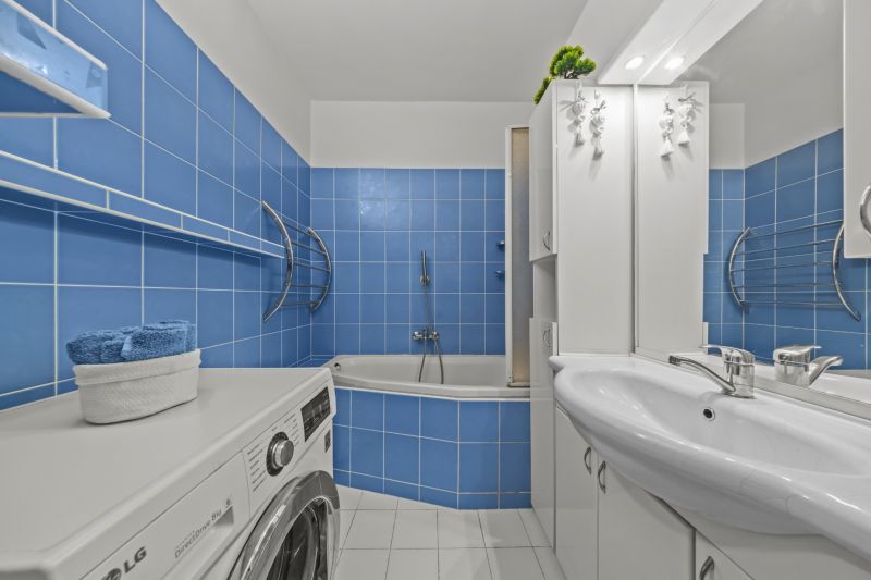 A bathroom with blue tiles, a bathtub, a washing machine, a sink, and storage space in a 3-room apartment.