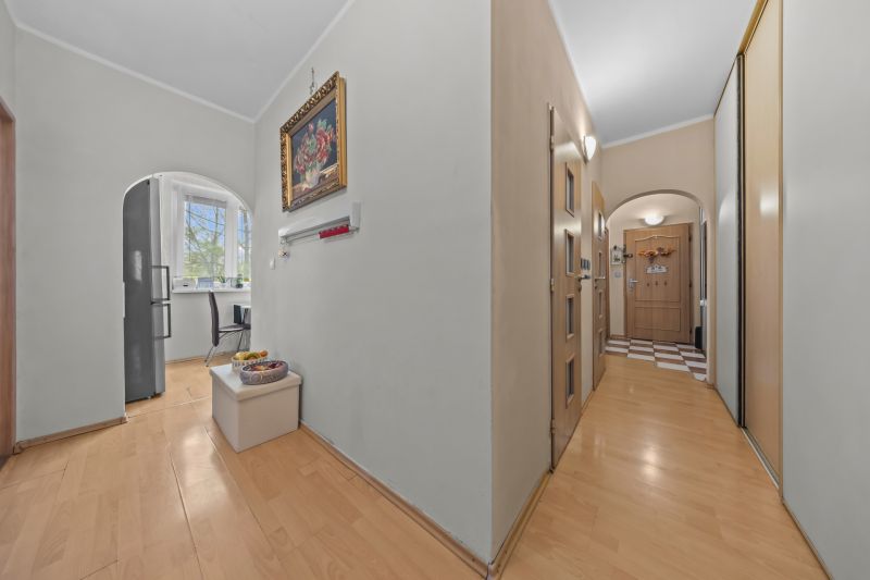 A hallway in a 3-room apartment with a wooden decor floor, a kitchen seen through an arch.