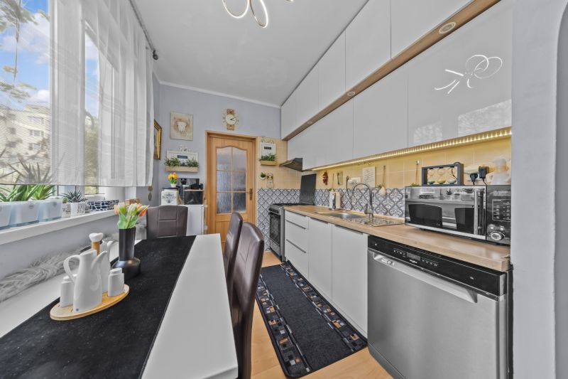 A kitchen in a 3-room apartment with a dining table, appliances, and white cabinets.