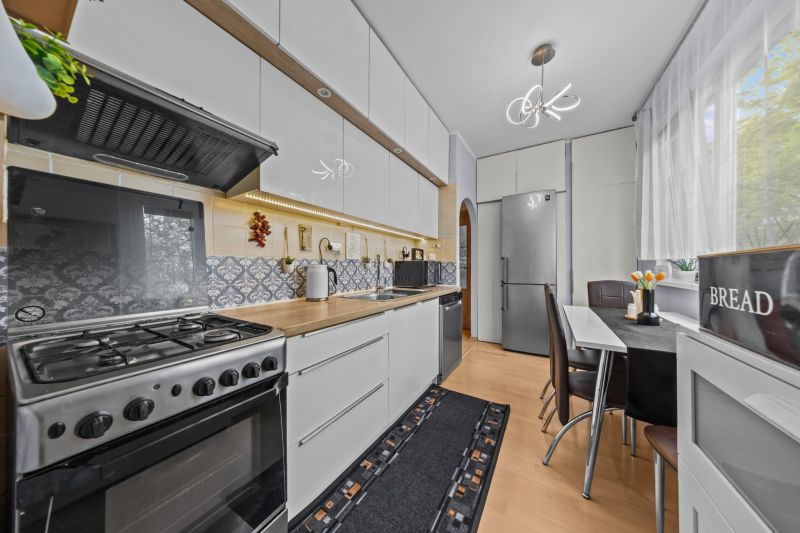 A kitchen with a stove, white cabinets, and a wooden decor floor in a 3-room apartment.