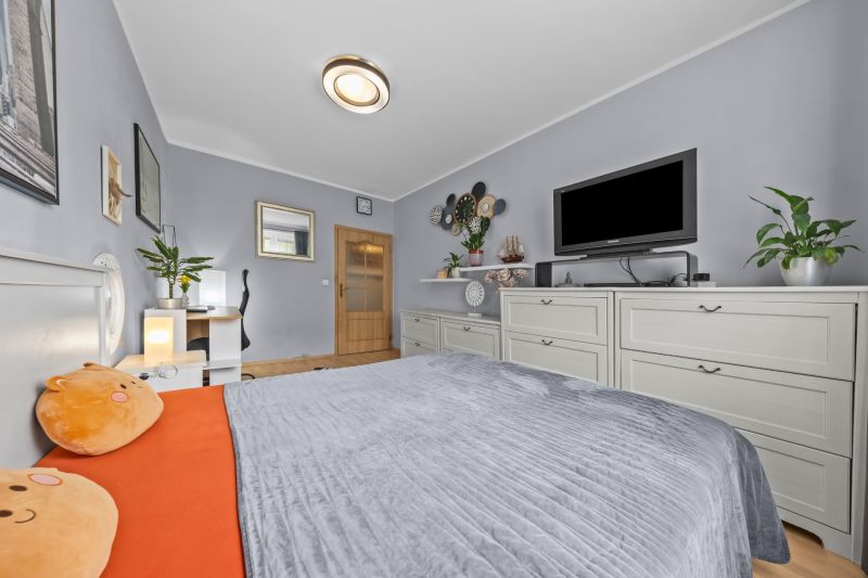A bright bedroom with a bed, television, decorations, and wood-patterned flooring in a three-room apartment.