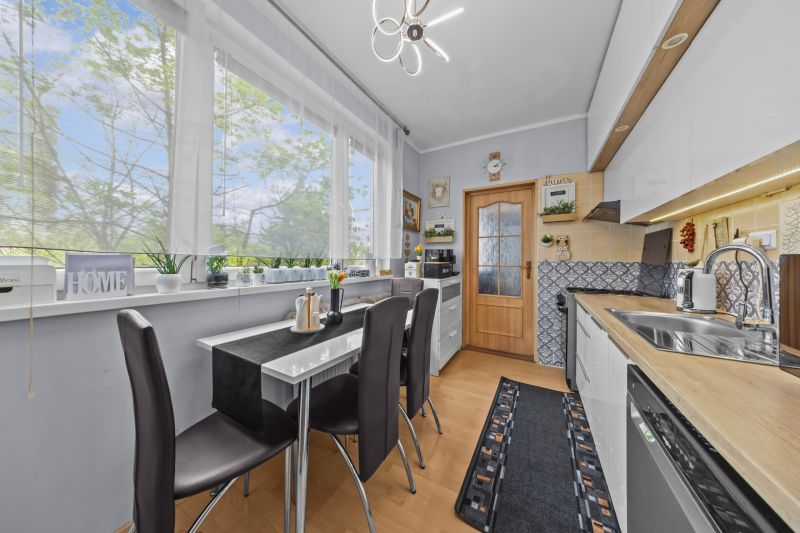 A kitchen table with chairs, plants on the windowsill, in a 3-room apartment, floor with wooden decor.