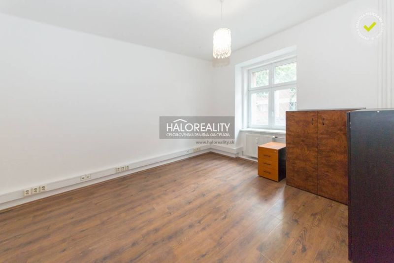 A room with a wooden floor, simple furniture, and a large window.