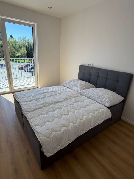 Bright bedroom in a 2-room apartment with wood-patterned flooring and a French window.