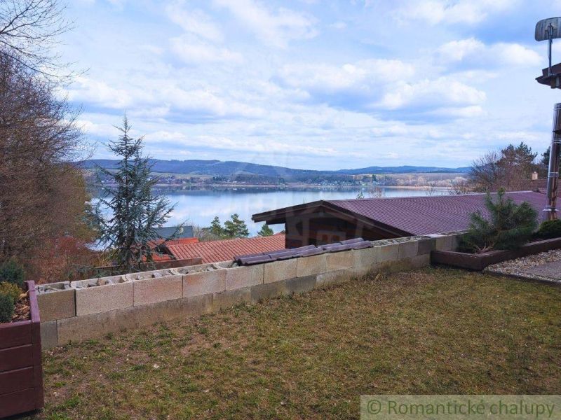 The view from the cottage in Kvakovce of the water surface surrounded by trees and hills.