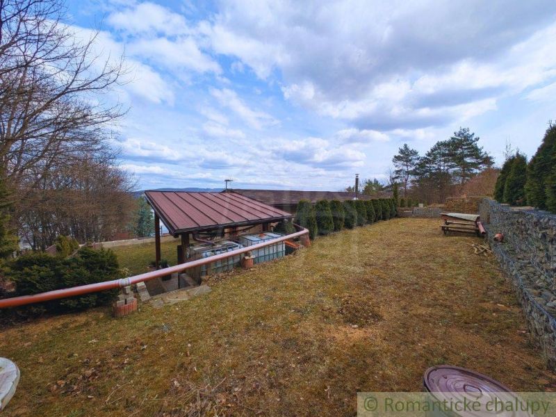 The exterior of the cottage in Kvakovce with a terrace and trees under a blue sky.