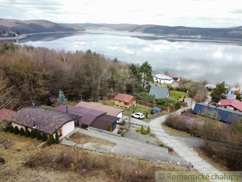 View of the lake in Kvakovce with cottages and green trees in the surroundings.