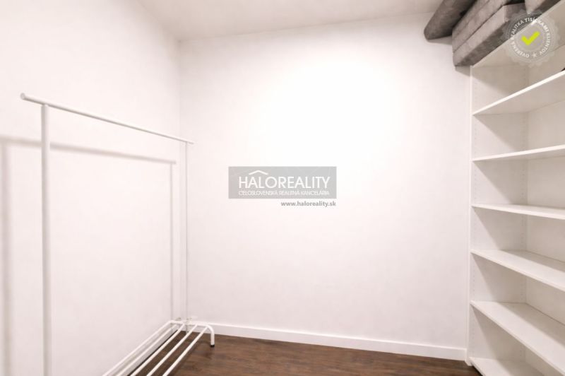 A white room with a clothes rack and shelves, floor with wood decor.