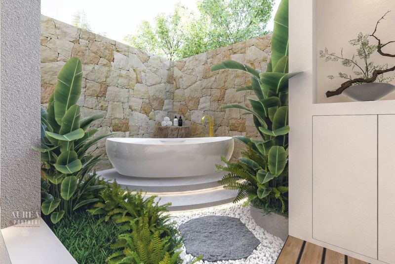 A bathroom in a villa with a freestanding bathtub, greenery, and a stone wall.
