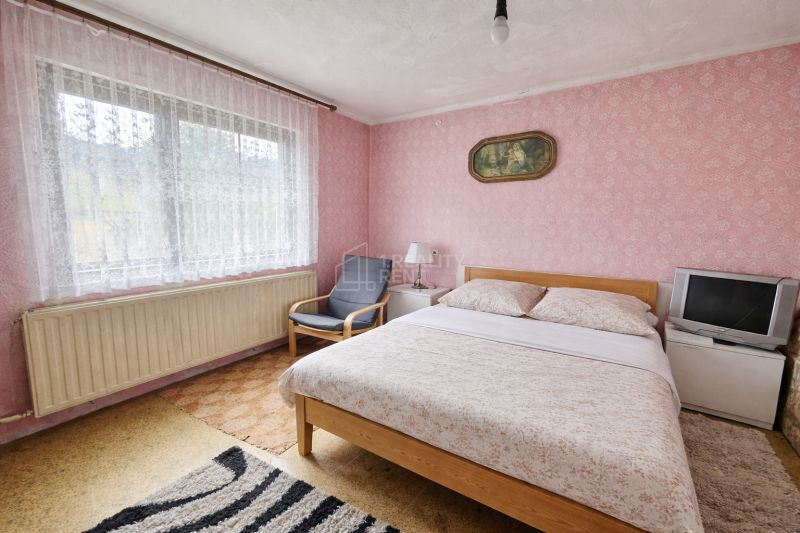 A room in a family house with a double bed, a television, and pink wallpaper.