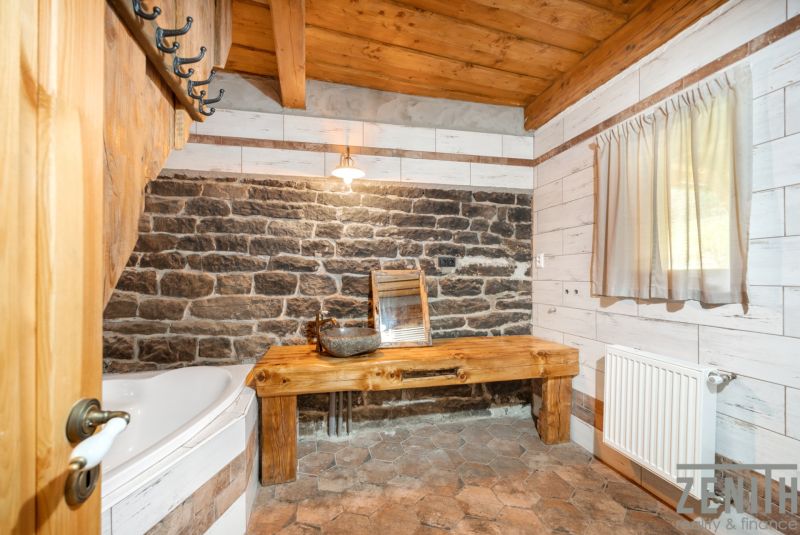 A bathroom in a family house with a stone wall, wooden ceiling, and rustic furnishings.