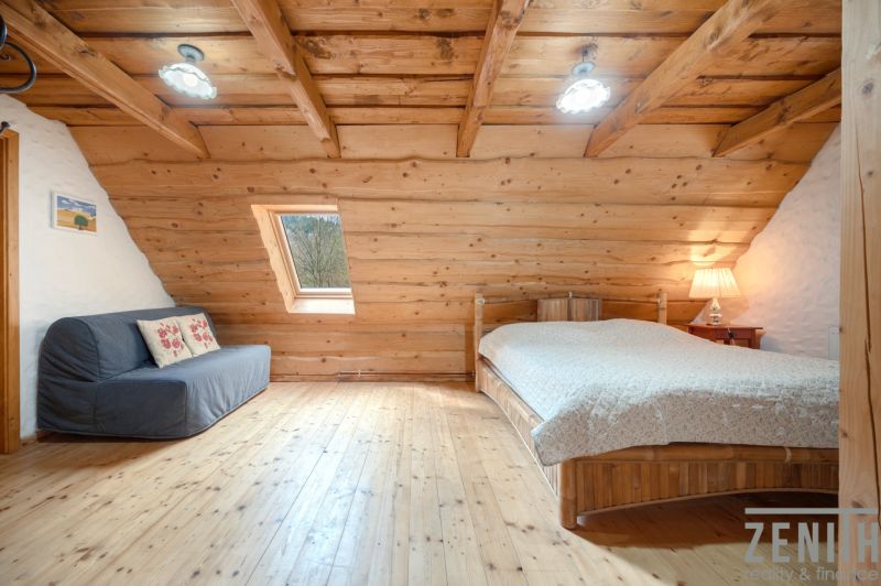 Attic room with wooden walls, a bed, and a sofa. Floor with wooden decor.