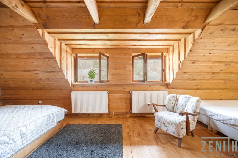 Attic room with wooden paneling, two beds, and an armchair, floor with wooden decor.