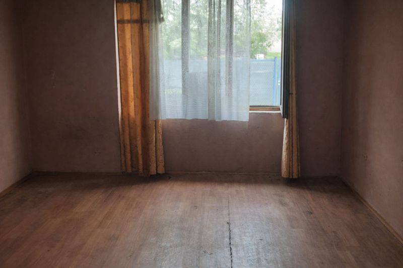 A room with a wooden floor design, curtains, and a window in a family house.