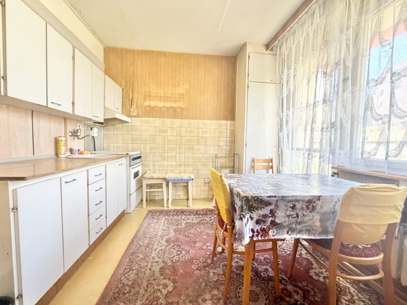 Kitchen in a 2-room apartment with a dining table, wooden cabinet decor, and curtains.