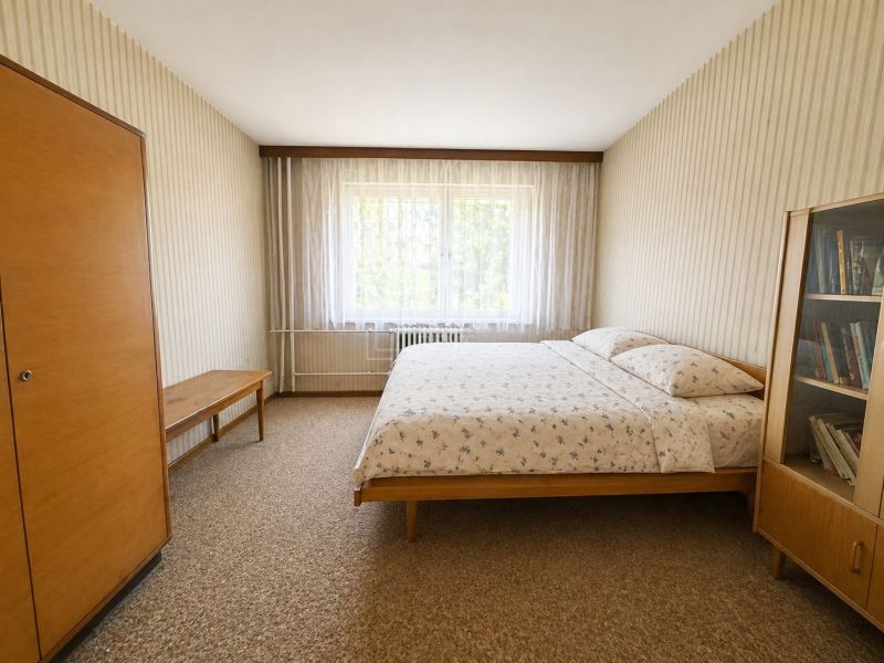 A bedroom in a two-room apartment with simple furniture and patterned wallpaper.