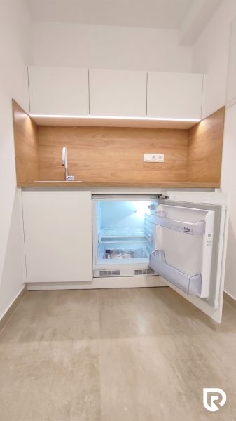 Kitchenette with a refrigerator, wooden decor flooring, and white cabinets in offices.