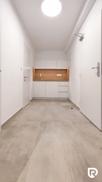 Minimalist white kitchen unit in an office with wood-decor flooring.
